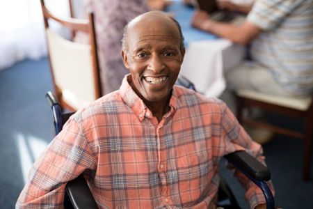 Portrait of smiling disabled senior man sitting on wheelchair at retirement homeの写真素材