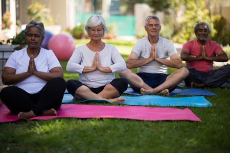 Multi ethnic senior people sitting in prayer position on yoga mats at parkの写真素材