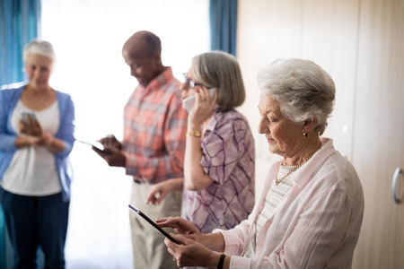 Seniors using technologies while standing against window at retirement homeの写真素材