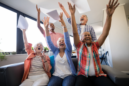 Excited senior people with arms raised throwing papers in nursing homeの写真素材