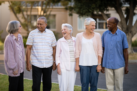Cheerful seniors standing while looking at each other against retirement homeの写真素材
