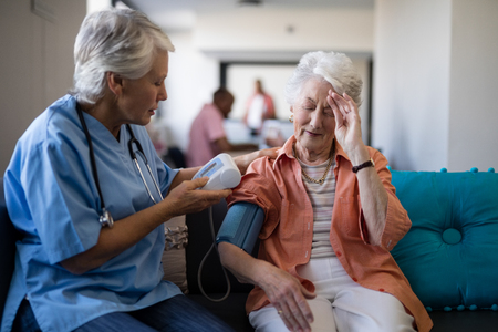 Senior woman complaining about headache to doctor during blood pressure check up at nursing homeの写真素材
