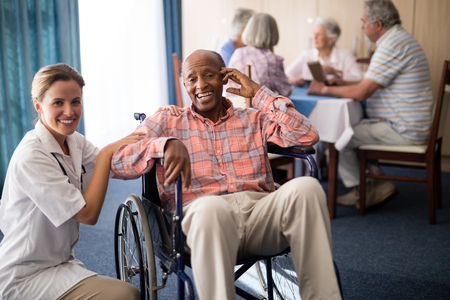 Portrait of cheerful disabled senior man sitting on wheelchair with female doctor at retirement homeの写真素材