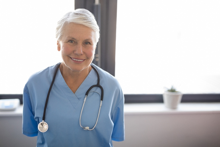 Portrait of senior female doctor standing against window in nursing homeの写真素材