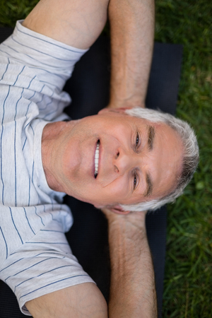 High angle portrait of smiling senior man resting while lying on exercise mat at parkの写真素材