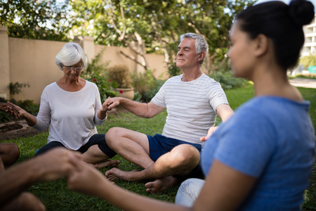 Senior people holding hands and meditating with trainer at parkの写真素材