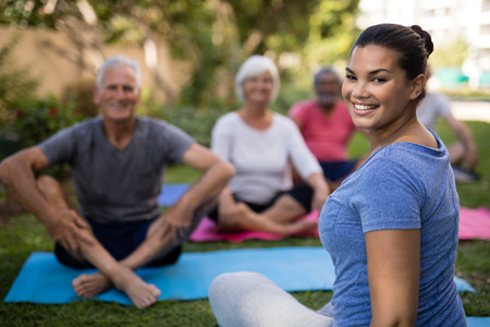 Smiling trainer sitting with senior people while exercising at parkの写真素材