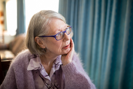 Thoughtful senior woman looking away while sitting in nursing homeの写真素材