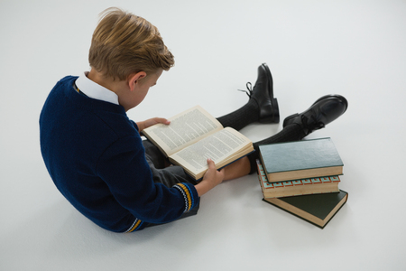 Attentive schoolboy reading book on white backgroundの写真素材