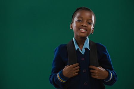Smiling school girl with backpack standing against chalk boardの写真素材