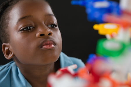 Attentive schoolgirl experimenting molecule model against black background