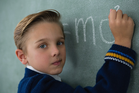 Portrait of schoolboy writing maths formula on chalkboard