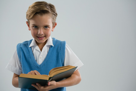 Portrait of schoolboy reading book against white backgroundの写真素材