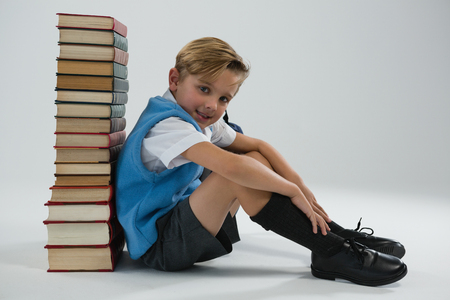Portrait of schoolboy sitting against books stack on white backgroundの写真素材