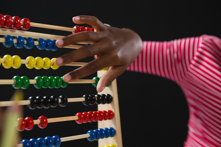 Mid-section of schoolgirl using abacus against black backgroundの写真素材