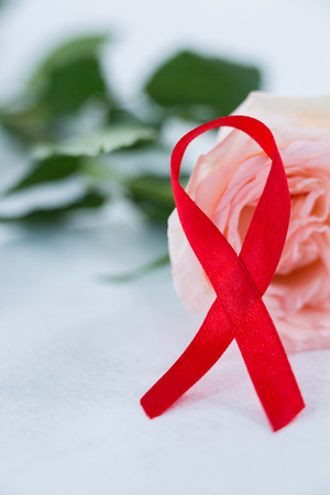 Close-up of red AIDS ribbon with pink rose on white backgroundの写真素材