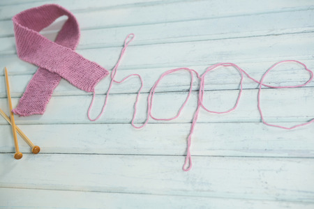 High angle view of pink Breast Cancer Awareness ribbon by hope text and crochet needles on white wooden tableの写真素材