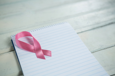 High angle view of pink Breast Cancer Awareness ribbon and spiral notepad on wooden tableの写真素材