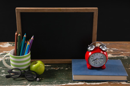 Chalkboard with book, pen holder, apple and spectacles on wooden tableの写真素材