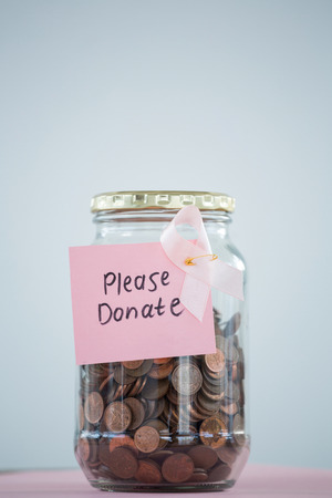 Close-up of card and pink Breast Cancer Awareness ribbon on jar with coins against white backgroundの写真素材