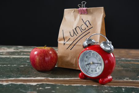 Close-up of apple, alarm clock and lunch bag on wooden tableの写真素材
