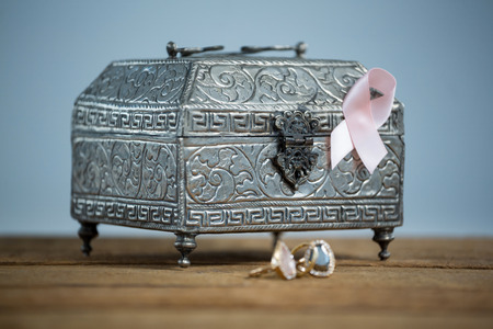 Surface level view of pink Breast Cancer Awareness ribbon with chest and rings on wooden table...