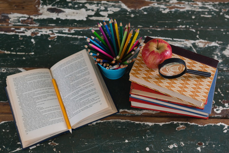 Stack of books with magnifying glass, apple and pen holder on wooden tableの写真素材