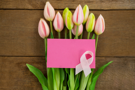 Overhead view of pink Breast Cancer Awareness ribbon with blank card on tulips over wooden tableの写真素材