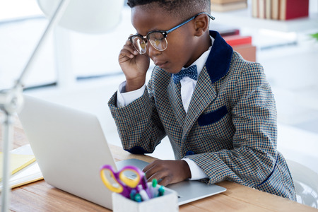 Kid Businessman wearing eyeglasses while using laptop at desk in officeの写真素材