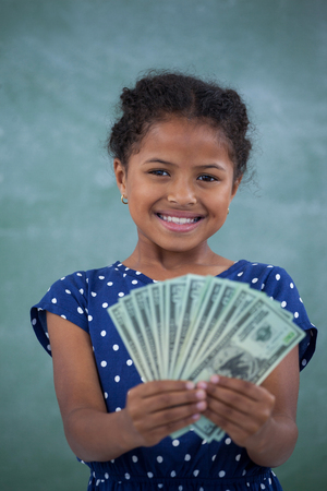Close up portrait of smiling girl showing paper currency against wallの写真素材