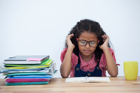 Kid Businesswoman reading book while sitting at desk against white backgroundの写真素材