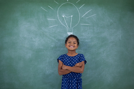 Happy girl with arms crossed standing by bulb drawing on gray wall