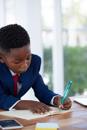 kid Businessman writing on diary at desk in officeの写真素材