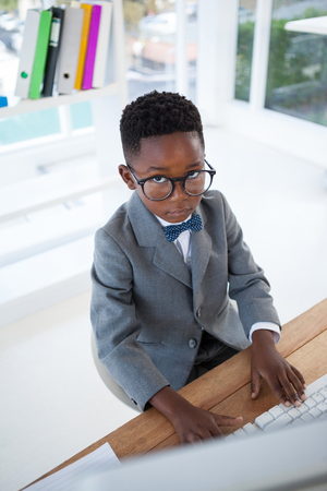 High angle portrait of kid businessman using computer at desk in officeの写真素材