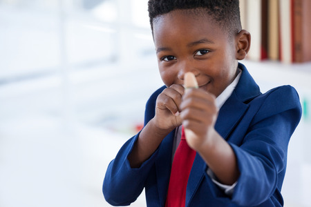 Portrait of boy imitating as businessman playing with rubber band while standing in officeの写真素材