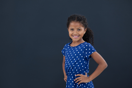 Portrait of girl with hand on hip standing against black backgroundの写真素材