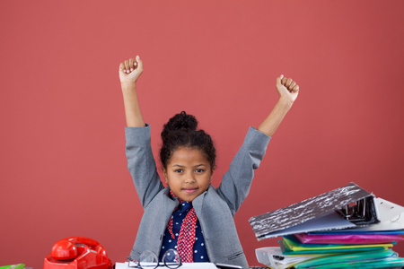Portrait of kid businesswoman stretching while sitting at desk against orange backgroundの写真素材