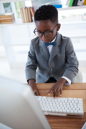 High angle view of kid businessman wearing eyeglasses using computer while working in officeの写真素材