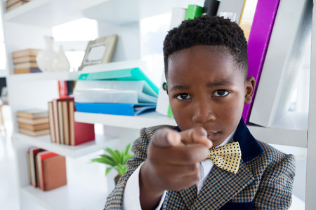 Portrait of kid businessman pointing while standing by shelf in officeの写真素材