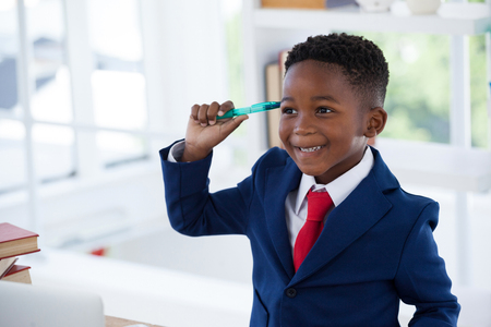 Close up of smiling kid businessman holding pen while looking awayの写真素材
