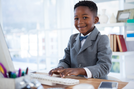Portrait of boy imitating as businessman using computer at desk in officeの写真素材