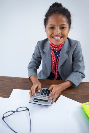 Portrait of smiling girl pretending as businesswoman using calculator while working at deskの写真素材