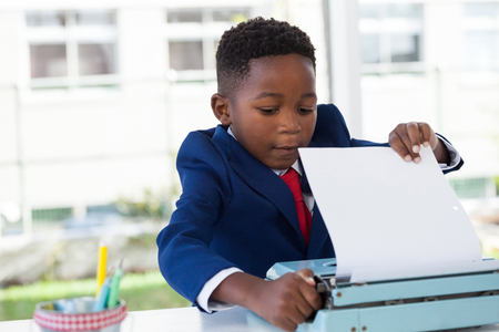 kid Businessman attaching paper in typewriter while working at table in officeの写真素材