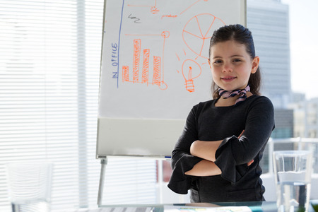 Portrait of smiling kid businesswoman with arms crossed standing by whiteboard in officeの写真素材