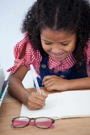 High angle view of smiling kid businesswoman writing on book at desk in officeの写真素材