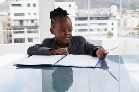 Smiling businesswoman with file and pen sitting at conference table in officeの写真素材