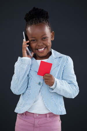 Portrait of cheerful businesswoman talking on phone while holding red card against gray wall in officeの写真素材
