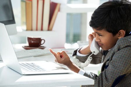 Businessman talking through telephone while pointing on laptop at desk in officeの写真素材