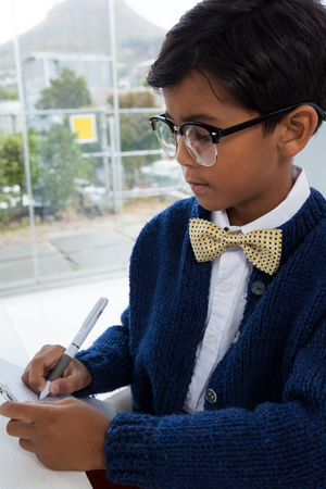Close up of businessman writing on paper while sitting by window in officeの写真素材