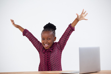 Portrait of cheerful woman with arms raised by laptop at desk in officeの写真素材